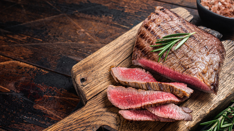 Sliced flank steak on a cutting board garnished with herb