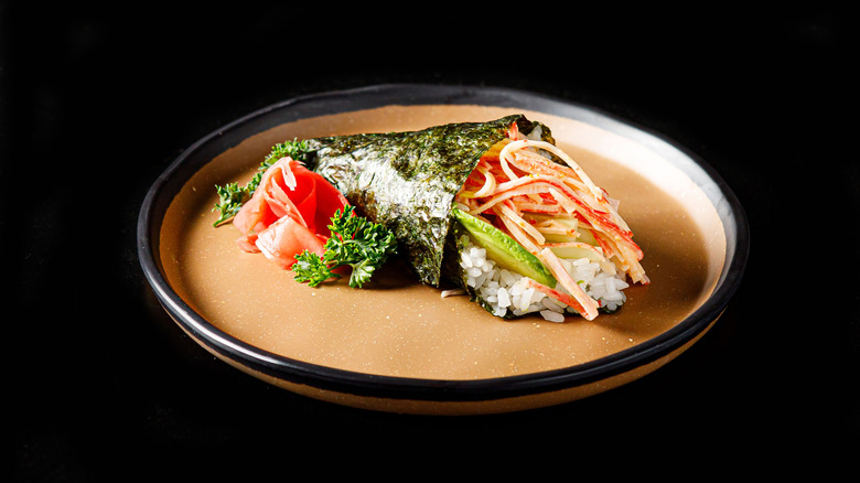 A piece of temaki, filled with rice and ikura, on a rectangular black plate.