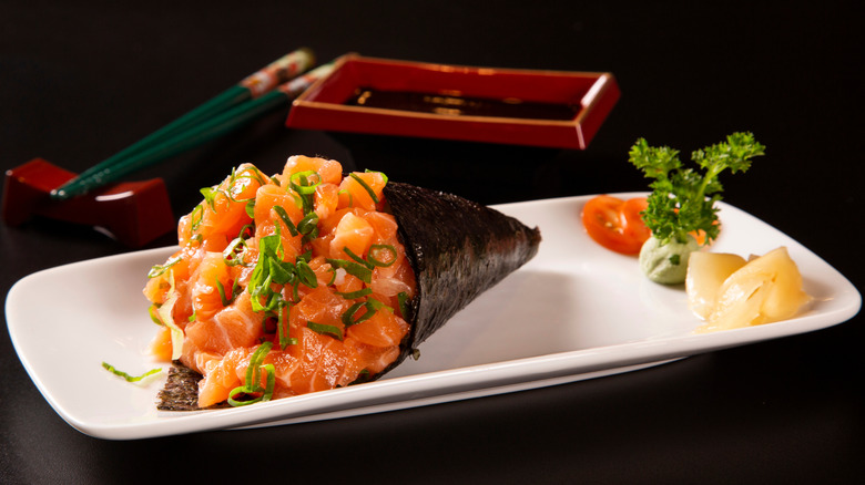 A salmon temaki on a white plate with condiments.