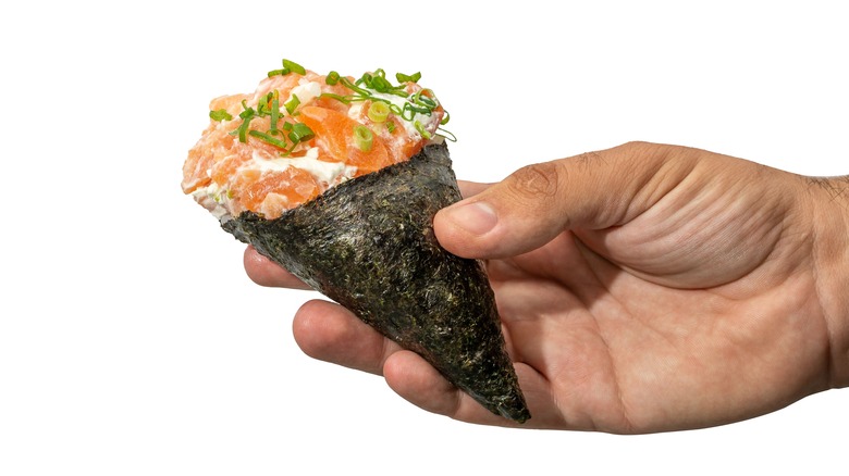 A hand holding a piece of temaki sushi