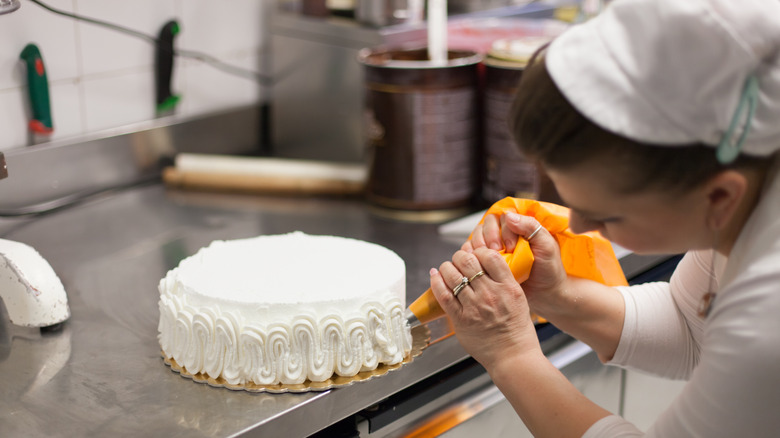 A pastry chef frosts a cake on a bakery countertop.