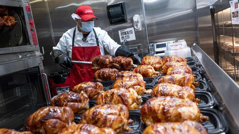 Costco employee prepares rotisserie chicken in plastic trays