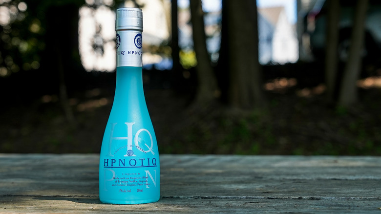 A bottle of Hpnotiq on cement with a woodsy background