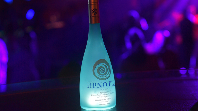 A bottle of Hpnotiq on a black bar counter with a trendy purple background