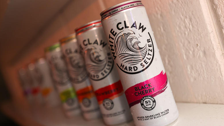 A line of white claw cans in various flavors sit against a white brick wall