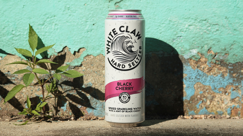 A black cherry flavored can of White Claw is set against a background of chipped teal paint