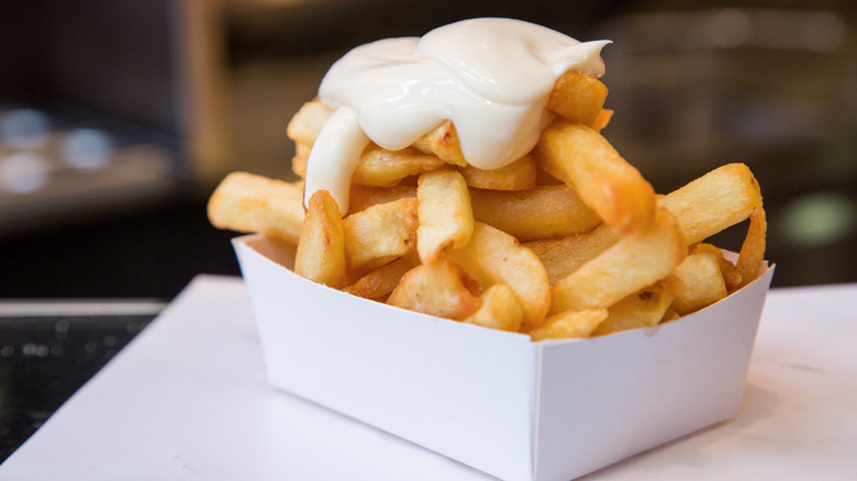 A paper plate of Belgian fries with mayonnaise on top