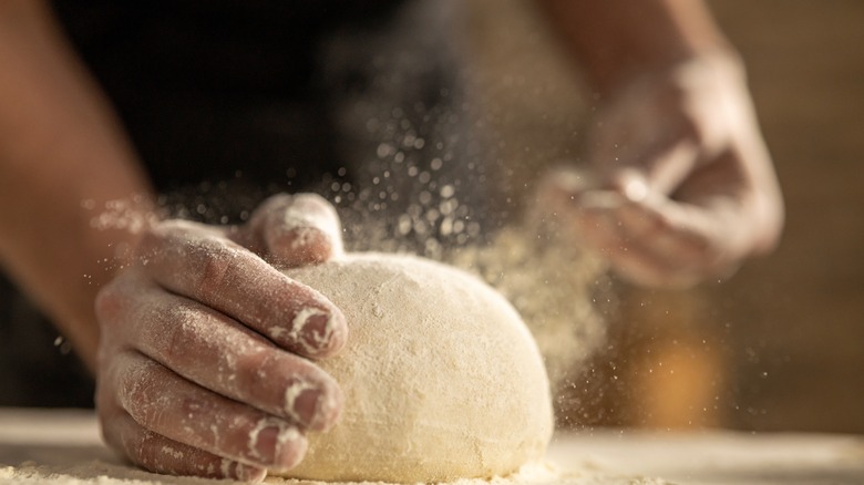 Hands kneading bread dough with flour