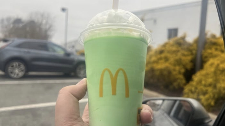 Hand holding a green McDonald's Shamrock Shake in a parking lot