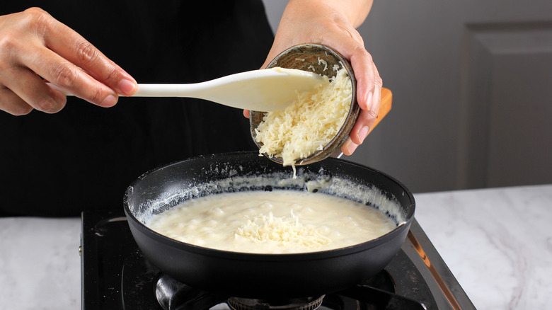 Adding shredded cheese to bechamel sauce in pan