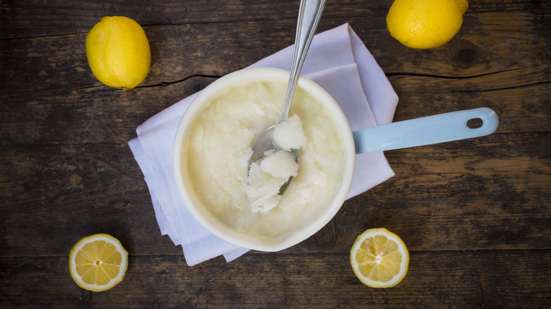 A pan full of lemon water ice with silver spoon and lemons on dark table