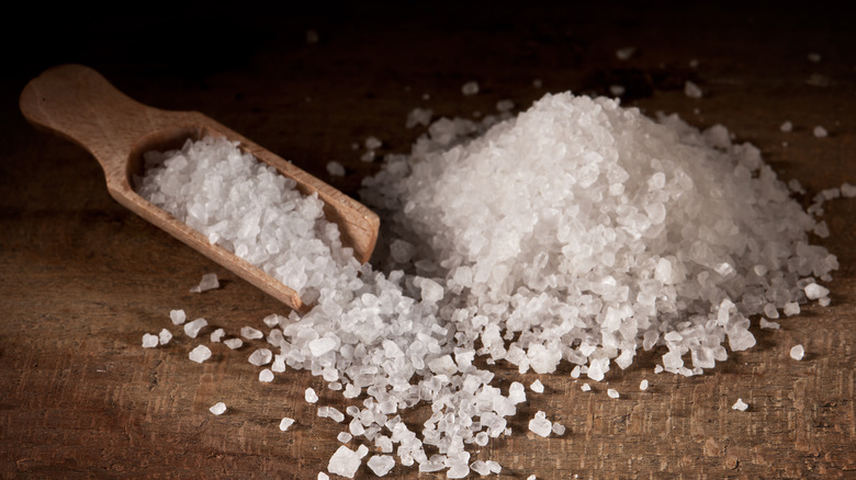 Coarse salt in a mound and in a wooden spoon on a brown surface