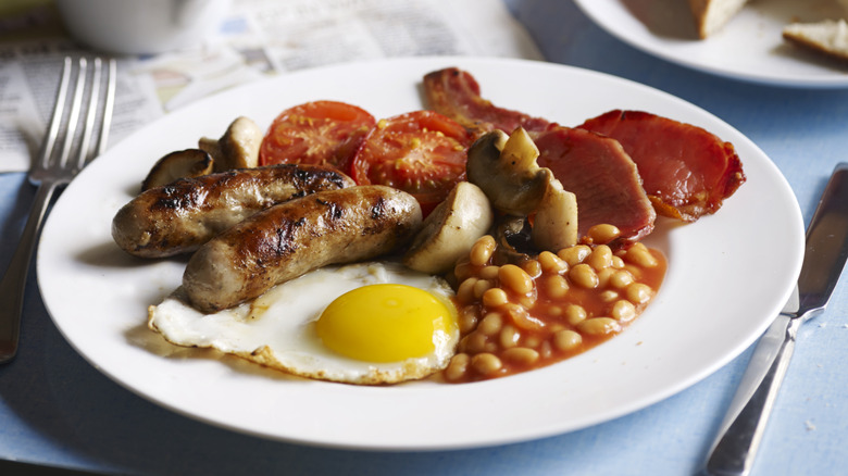 White plate with sausages, eggs, beans, tomatoes, and bacon