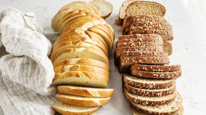 Two rows of white bread and whole wheat bread on a counter next to a white cloth