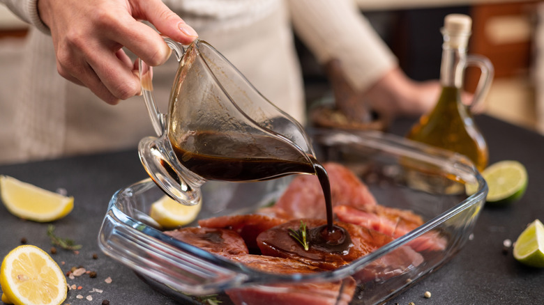 Hand pouring dark soy sauce marinade over meat