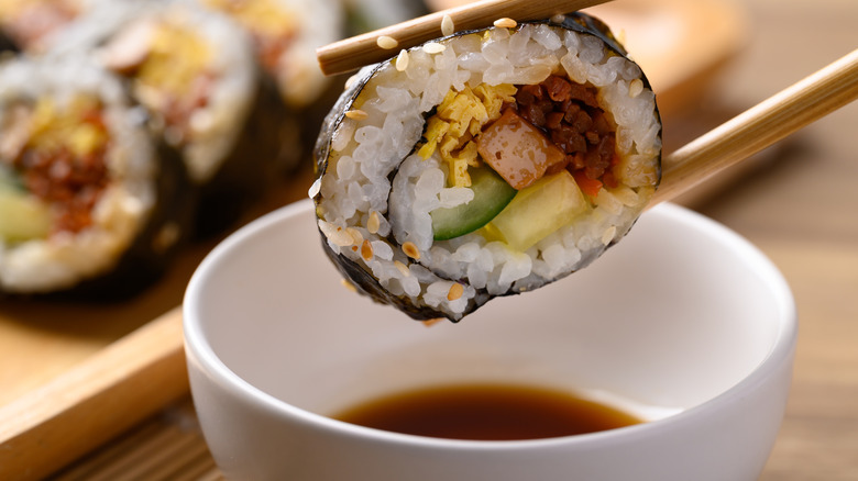 Sushi being dipped in light soy sauce in white bowl