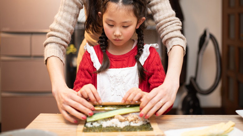 Woman assisting child making sushi rolls