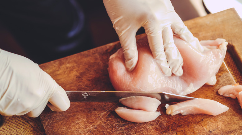 Gloved chef slicing chicken breast