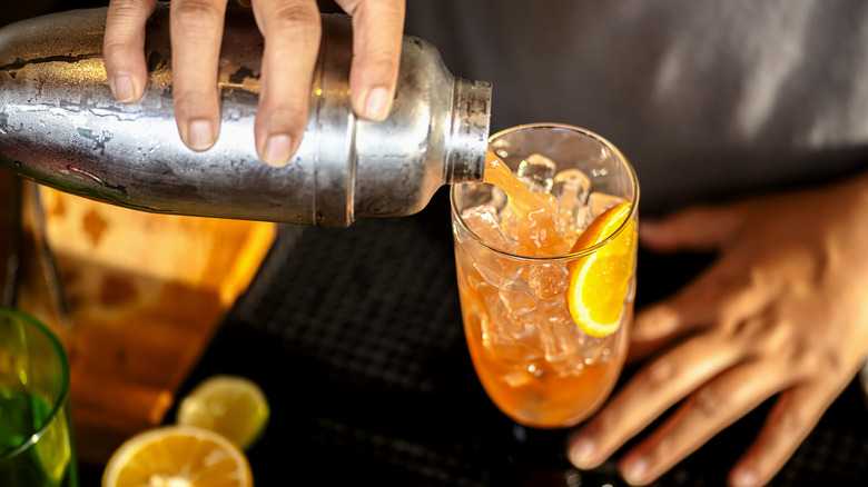 Drink being poured from a cocktail shaker into a glass with ice