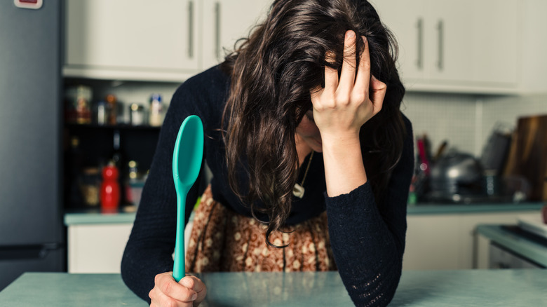 Person in a kitchen holding a turquoise mixing spoon puts their hand to their head in frustration