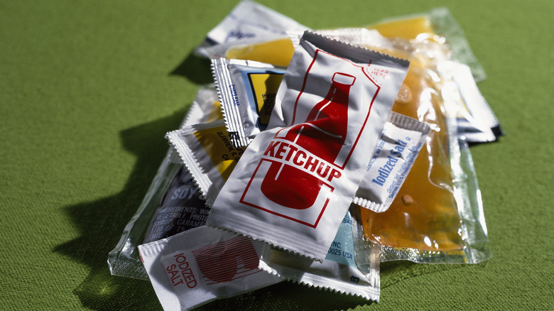 Pile of condiment packets including ketchup, salt, and soy sauce, lie on a green background