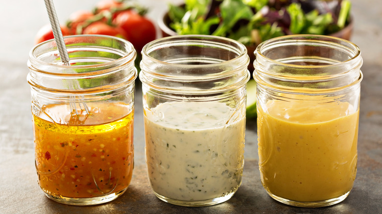 Three different flavors of homemade salad dressings sit in glass mason jars