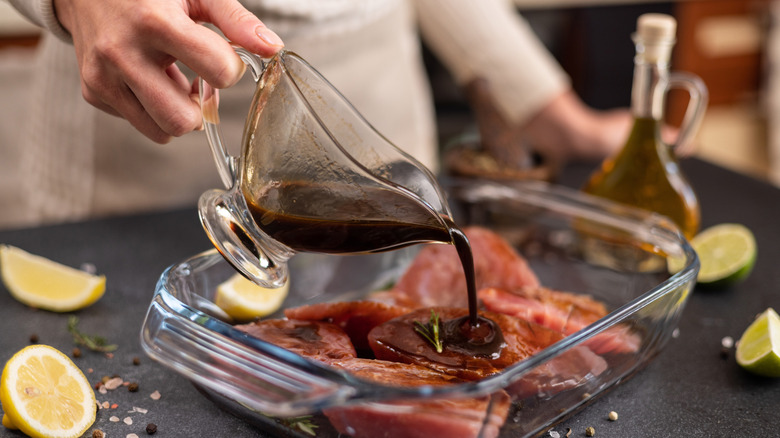 Person pouring a brown-colored marinade over meat in glass tray