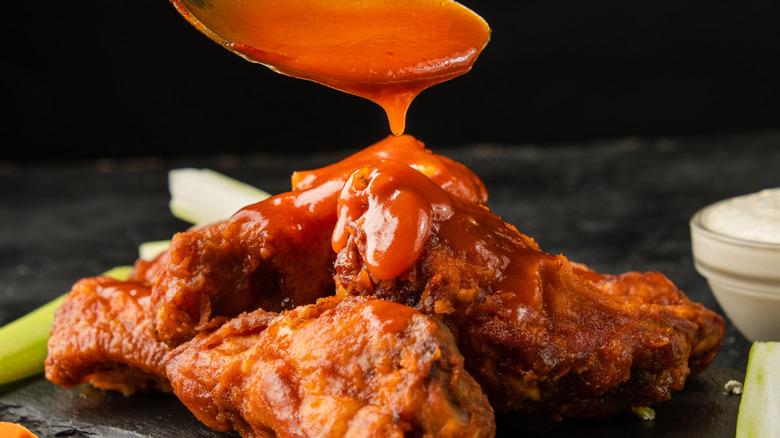 A spoonful of buffalo sauce is poured over chicken wings