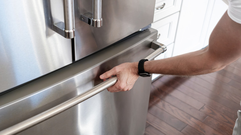 A person in the kitchen reaches down to open a stainless steel freezer door