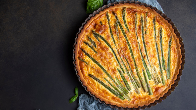 An asparagus and egg tart is in a pan on a grey background.