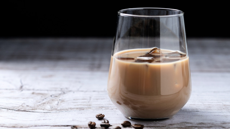 A glass of coffee liqueur on ice sits on a surface with coffee beans