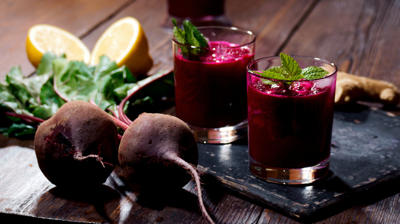 Beets sit next to two whiskey glasses of beet juice, garnished with mint