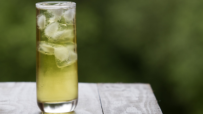 A tall glass of iced green tea sits on a wooden table outside