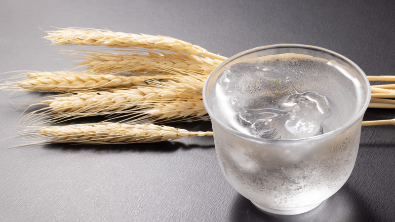 A small cup of Shochu rests next to several stems of barley wheat