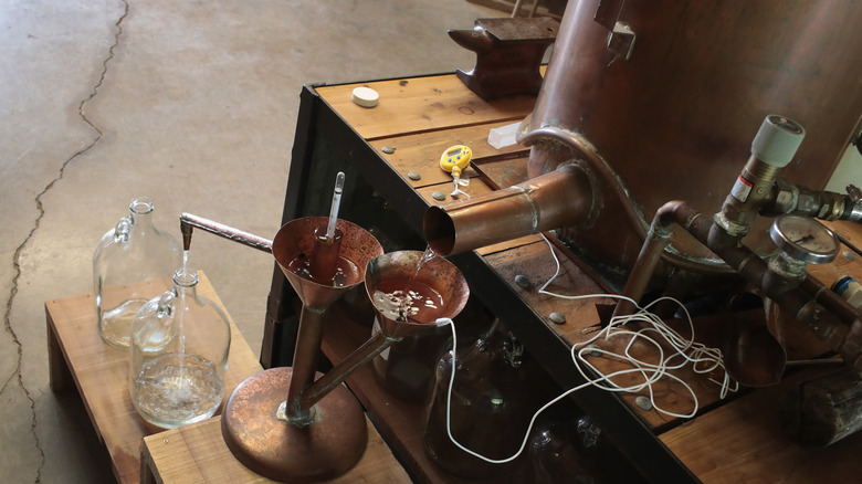 Moonshine runs from a still at a home distillery into a large glass jug