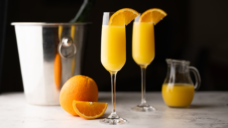 Two mimosas with orange juice and champagne in ice bucket