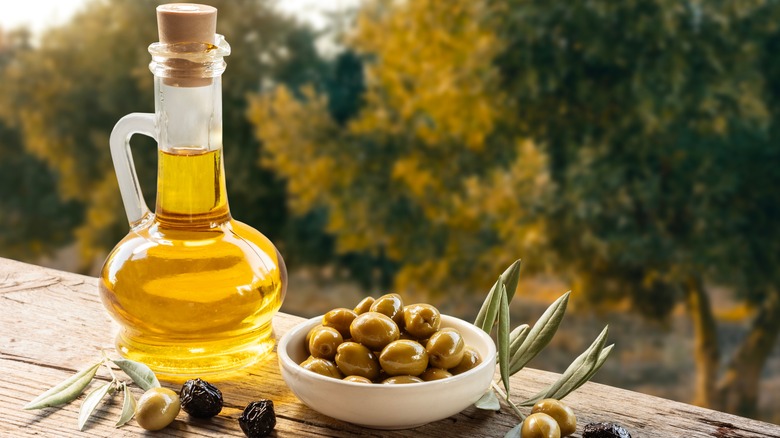 A bowl of olives and a carafe of olive oil on a wooden table outdoors