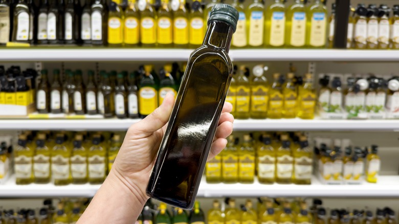 A person holds a dark bottle of olive oil in the oil aisle of the grocery store