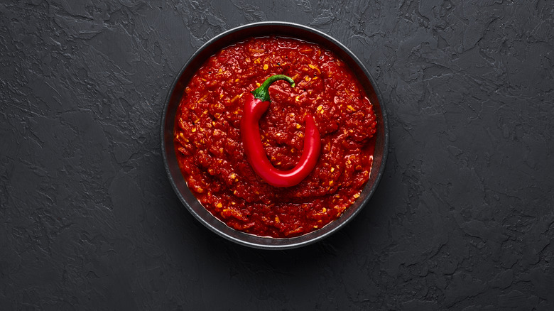 A tantilizing bowl of szechuan sauce topped with a chili pepper on a black granite table