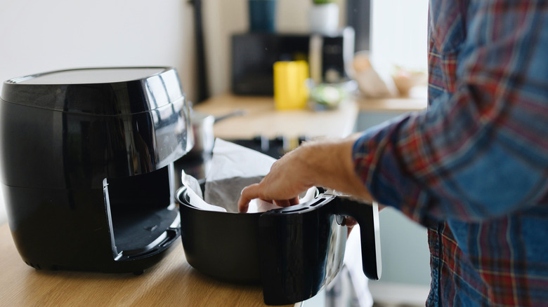 A man places a sheet of parchment paper into a black air fryer as a protective lining