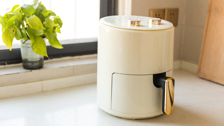 An attractive white and rose gold air fryer sits on a kitchen counter in a bright kitchen