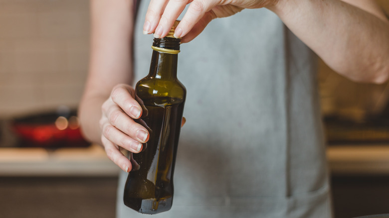 Hands holding dark glass olive oil bottle