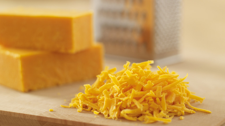 A pile of shredded cheddar next to two blocks of cheese