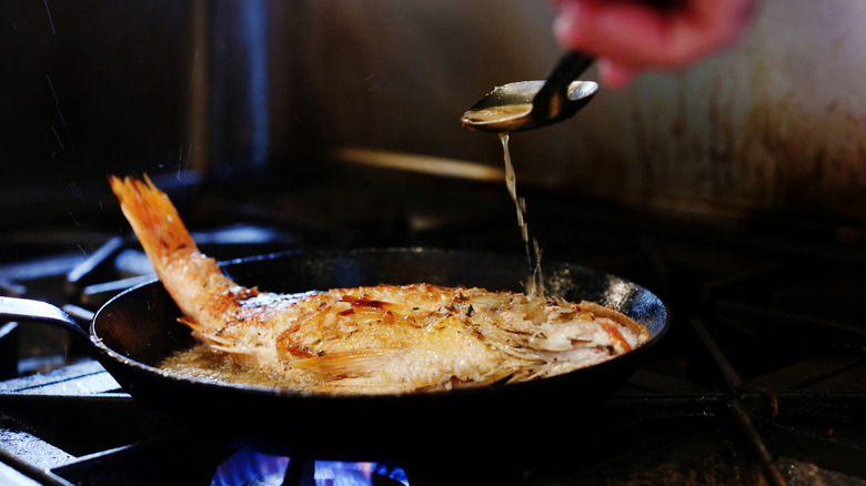 Chef spooning hot oil over a whole fried fish