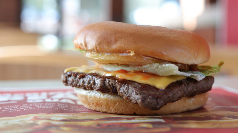 A Wendy's burger sits on a tray, stacked with lettuce, tomato, cheese, and sauce