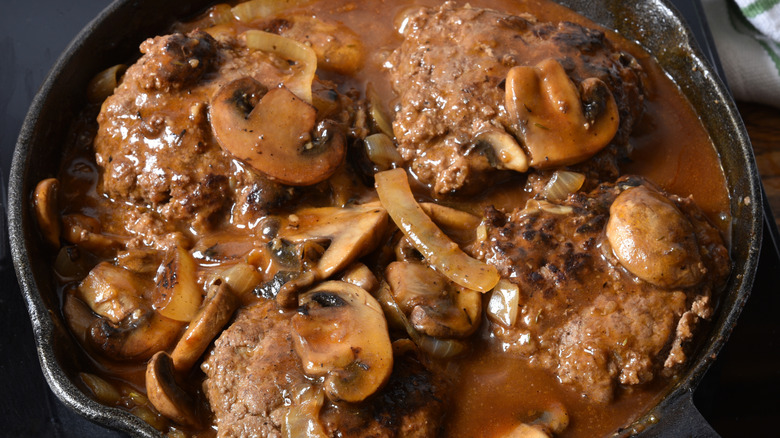 A cast iron skillet with four steaks smothered in mushroom gravy cooking