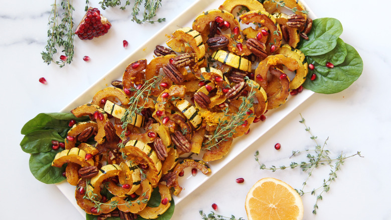 Sliced cooked delicata squash served with pomegranate seeds and orange on a white platter