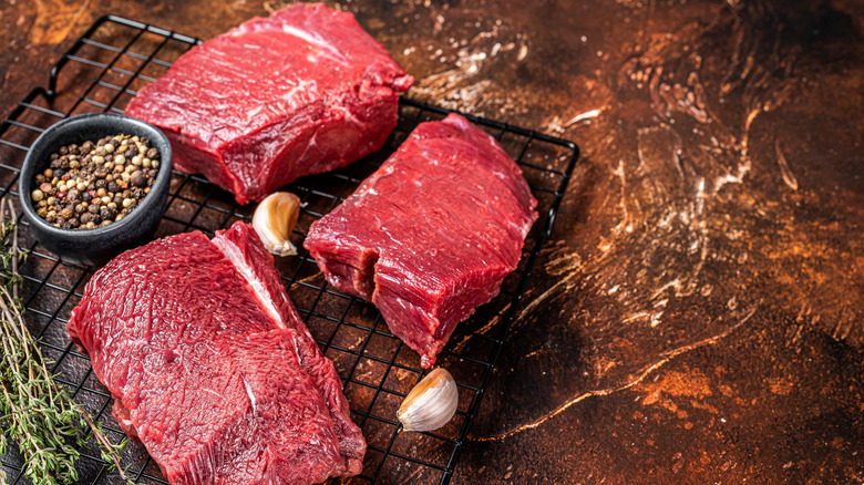 Slabs of venison next to garlic, peppercorns, and thyme