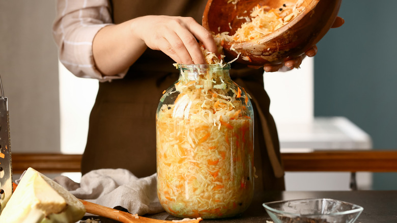 woman filling large jar with sauerkraut