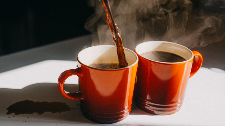 Two red cups with steaming coffee being poured into the one on the left